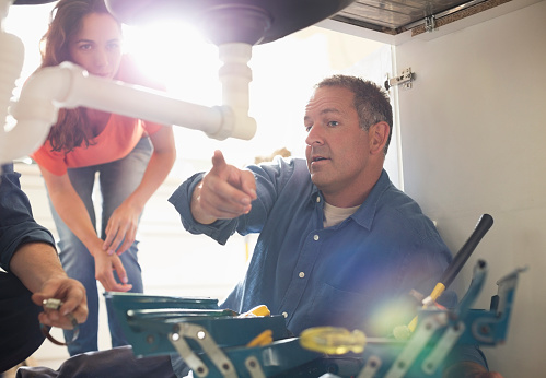 Plumber showing a woman the pipe leak under the sink